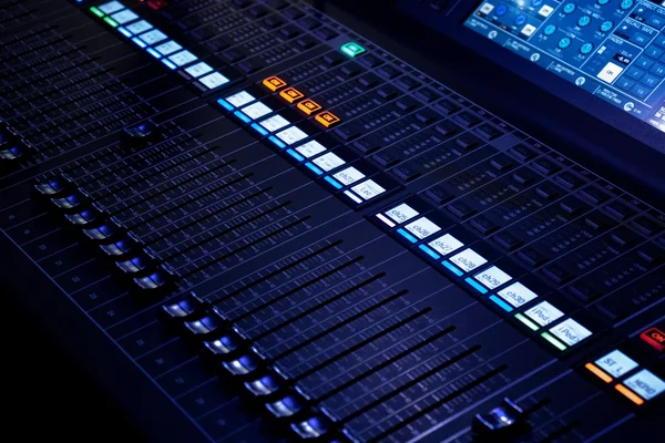 Wide view of an audio mixing console with rows of faders and controls.