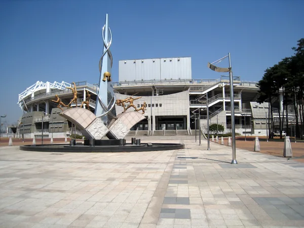 Exterior of Goyang Stadium in South Korea, including its entrance plaza, sculpture and grandstand.