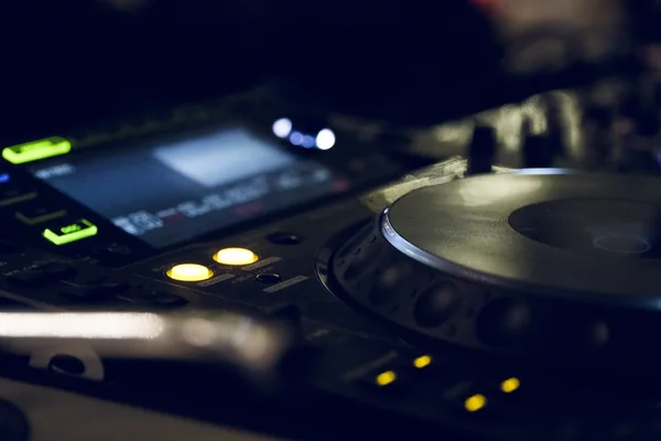 Close-up of a DJ turntable and illuminated controls in a dark booth.